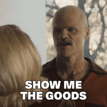 a man with a mustache is talking to a woman and says " show me the goods "