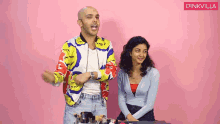 a man in a colorful jacket is standing next to a woman in a blue top .