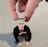a person is holding a small man with green hair and red nails .