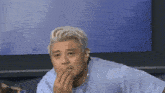 a man in a blue shirt is covering his mouth with his hand .
