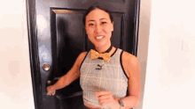 a woman wearing a bow tie and a crop top is opening a door .