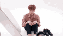 a man in a pink shirt is sitting on the floor next to a pair of shoes .