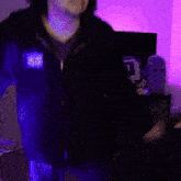 a person in a dark room with a purple light behind them and a person wearing blue shorts with the letter h on them