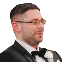 a man wearing glasses and a tuxedo has a white flower in his pocket