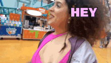 a woman in a pink top is standing in front of a snacks and drinks stand and says hey