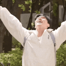 a young man with his arms outstretched is wearing a white jacket with the word adidas on it .