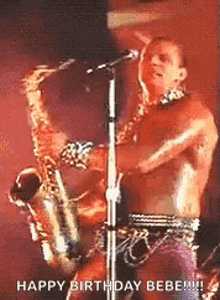 a man without a shirt is playing a saxophone in front of a microphone .
