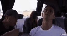 a man in a white shirt is sitting on a bus talking to another man in a hat .
