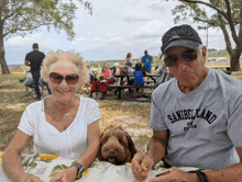 a man wearing a shirt that says sanibelland is sitting next to a woman and a dog