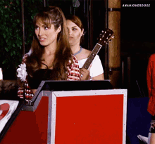 a woman holding a guitar in front of a red box with anahioverdose written on the bottom