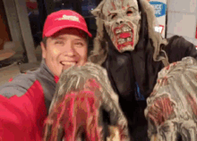 a man wearing a red hat with a smiley face on it poses with a zombie