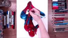 a person is drawing a picture of spider-man on a piece of paper surrounded by markers and pencils