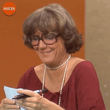 a woman wearing glasses and a pearl necklace smiles while holding a piece of paper