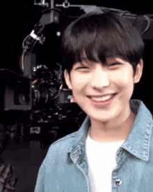 a young man wearing a denim jacket and a white shirt is smiling in front of a camera .