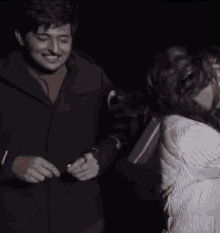 a man and a woman are kissing in a dark room . the woman is wearing a white jacket .
