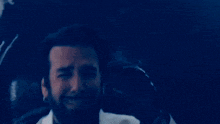 a man with a beard wearing a white suit and black shirt is holding a remote control .