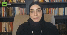a woman wearing a hijab is sitting in front of a bookshelf with rt india written on the bottom