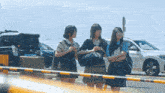 three girls standing in front of a barrier with a car in the background