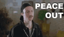 a man with a mustache is sitting in a living room with the words `` peace out '' written on the screen .