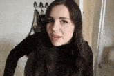 a woman wearing a black turtleneck sweater looks at the camera