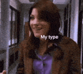 a woman in a brown jacket and purple shirt is standing in a hallway .