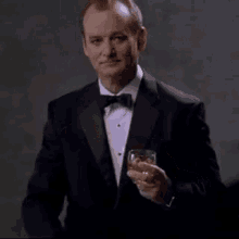 a man in a tuxedo and bow tie holds a glass of whiskey