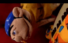 a stuffed animal with a blue hat and a yellow shirt is laying on its back next to a toy .