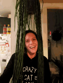 a woman wearing a crazy cat lady shirt holds a plant