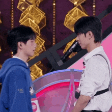 two young men are standing next to each other on a stage and talking to each other .