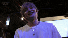 a man wearing a white t-shirt and a purple necklace is smiling .