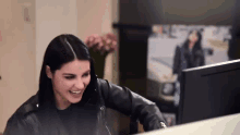 a woman in a leather jacket is sitting in front of a computer screen .