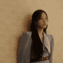 a woman in a blue dress is leaning against a wall and looking at the camera .