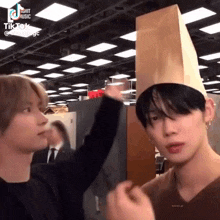 a man wearing a paper bag hat is touching another man 's head .