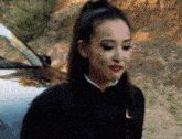 a woman in a black jacket is standing next to a car and making a funny face .