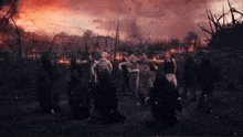 a group of people standing in a field with a fire in the background