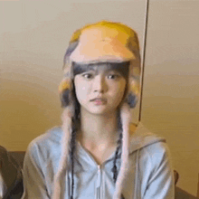 a young woman wearing a hat and a hoodie is sitting on a couch .
