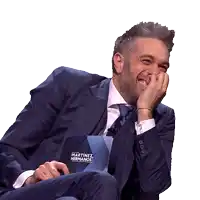 a man in a suit laughs while holding a martinez hermanos sign
