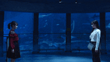 two women stand in front of a large aquarium