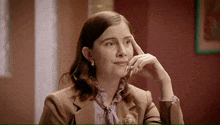 a woman in a brown suit is sitting at a table with her hand on her face .