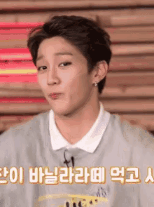 a young man is making a funny face in front of a sign that says ' korean ' on it .