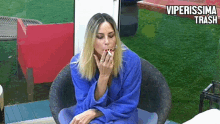 a woman wearing a blue robe is sitting in a chair smoking a cigarette .