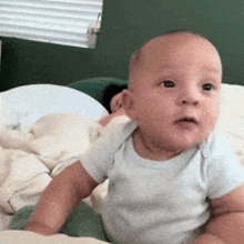 a baby in a white shirt is sitting on a bed looking at the camera