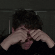 a man with curly hair is covering his face with his hands .