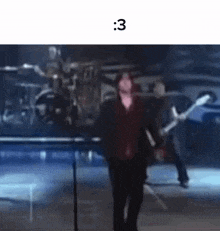 a man is walking on a stage in front of a band playing guitars .