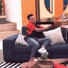 a man is sitting on a blue couch in a living room with polka dot pillows .