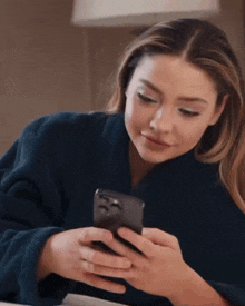 a woman in a blue robe looks at her phone