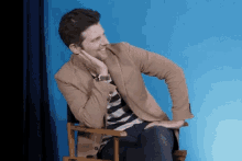 a man in a tan jacket is sitting in a director 's chair with his hand on his chin .