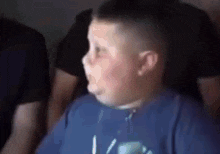 a young boy in a blue shirt is making a funny face while watching a video game .