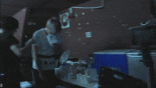 a man in a red shirt stands next to another man in a white shirt in a dark room