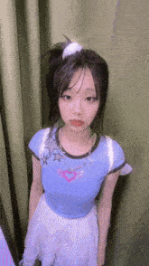 a young girl wearing a blue shirt and a white skirt is standing in front of a curtain .